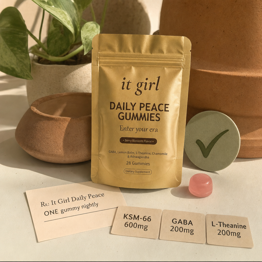 The real matte-gold It Girl Daily Peace pouch with a green checkmark, a single pink gummy, and three dose cards reading KSM-66 600mg, GABA 200mg, L-Theanine 200mg beside a now-filled prescription slip on a warm cream surface, the same script filled clean