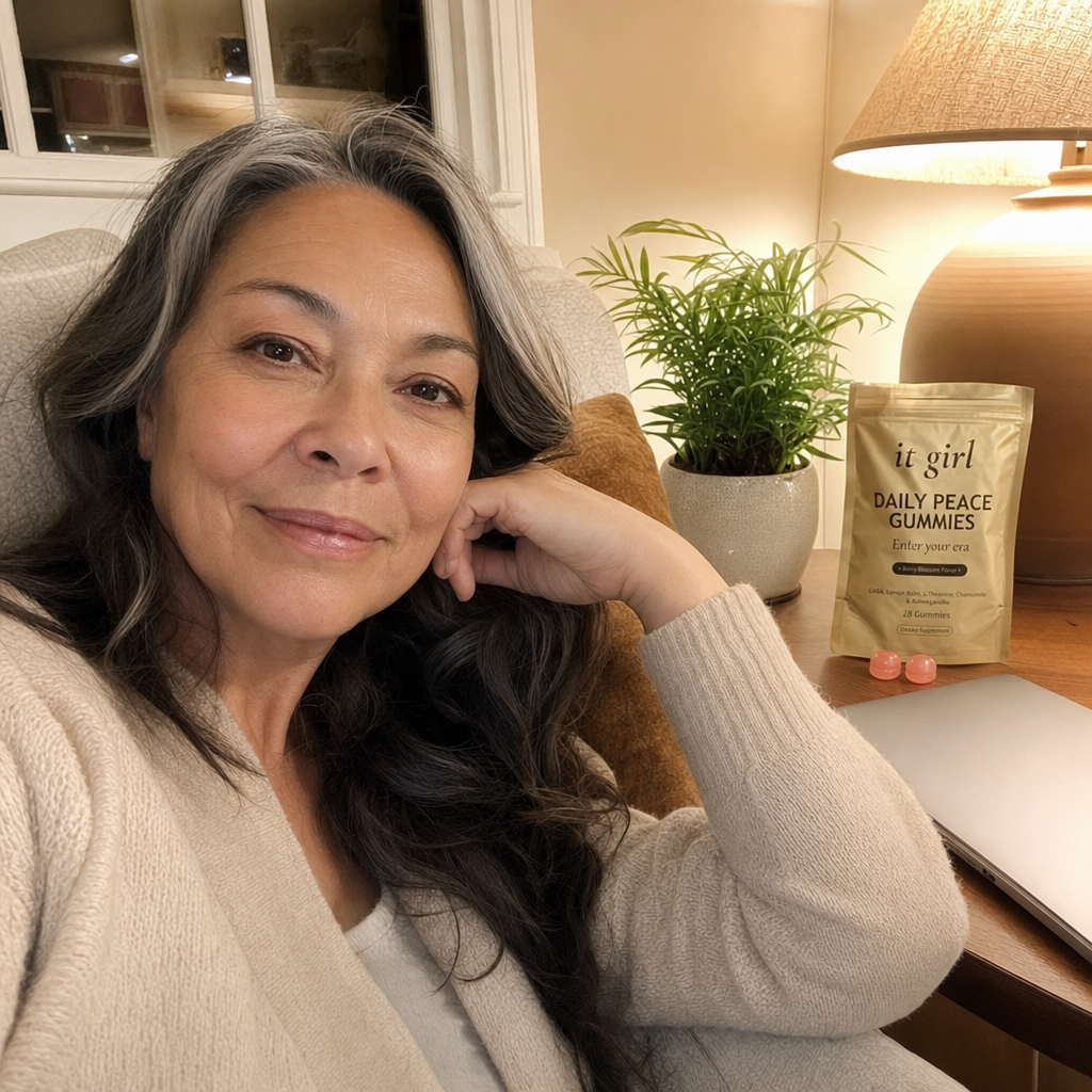 Real woman in her late fifties relaxed on her couch in the evening with the laptop closed, the gold It Girl Daily Peace pouch and a few gummies on the side table, the day finally letting go