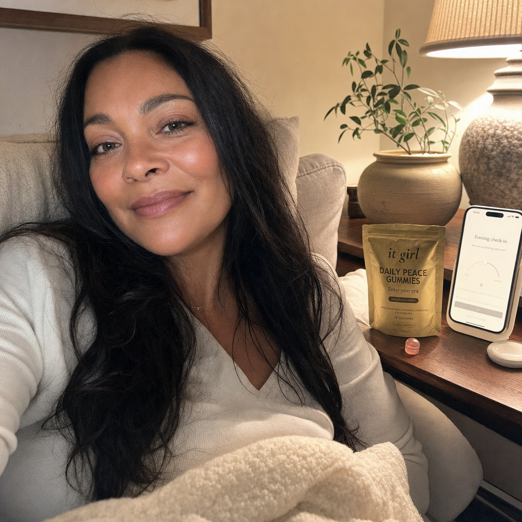 A calm woman settled on her couch in warm lamplight with the gold Daily Peace pouch and a phone showing a quiet evening calm check-in, calm that stays not sedation