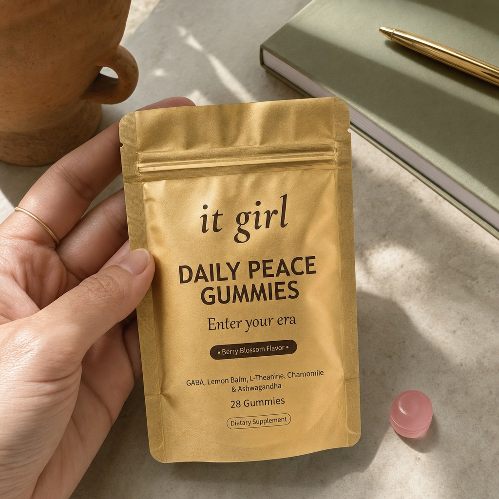 The real matte-gold It Girl Daily Peace pouch in warm daylight on a cream surface beside a single pink gummy, the thing built to rebuild the buffer rather than numb it