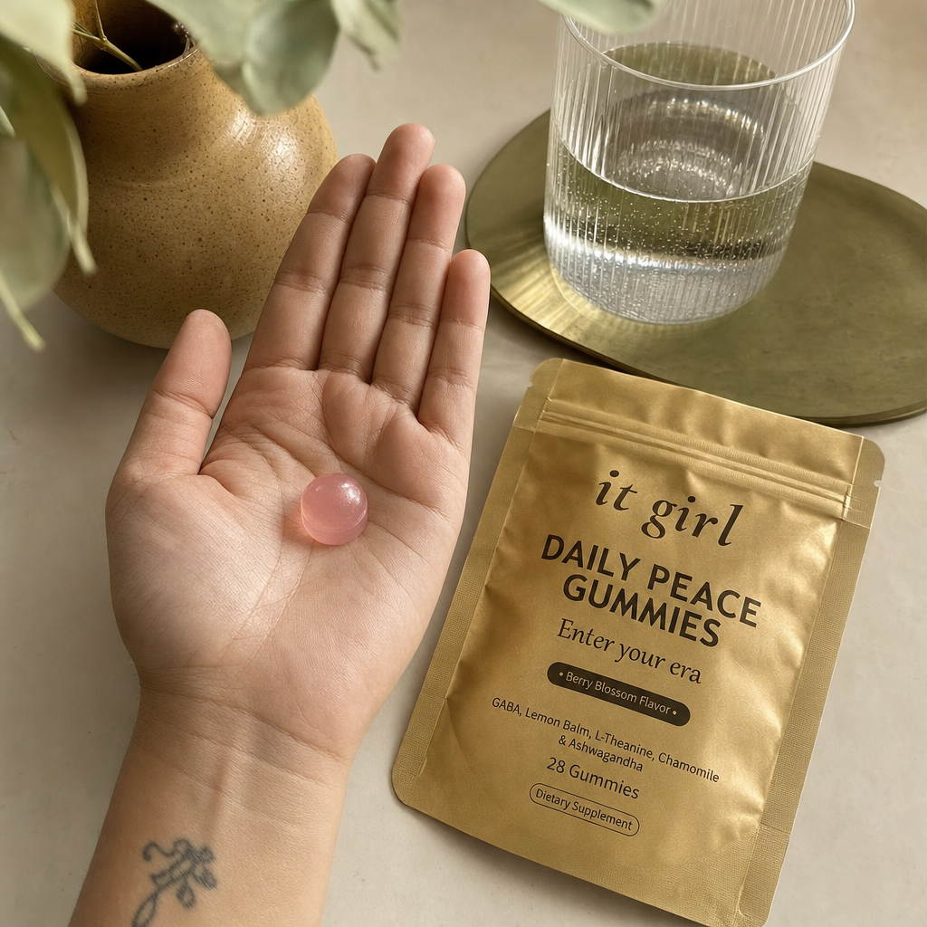 Open palm holding a single pink Daily Peace gummy beside the gold pouch and a glass of water on a cream counter, the GABA and L-Theanine calm signal handed back