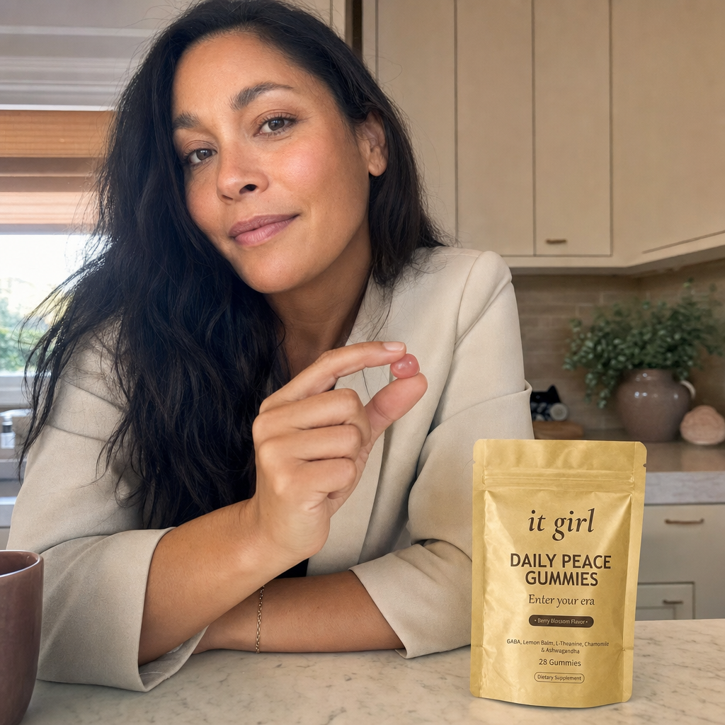 A calm put-together woman in her forties at her morning kitchen counter holding a single gummy with the gold Daily Peace pouch beside her