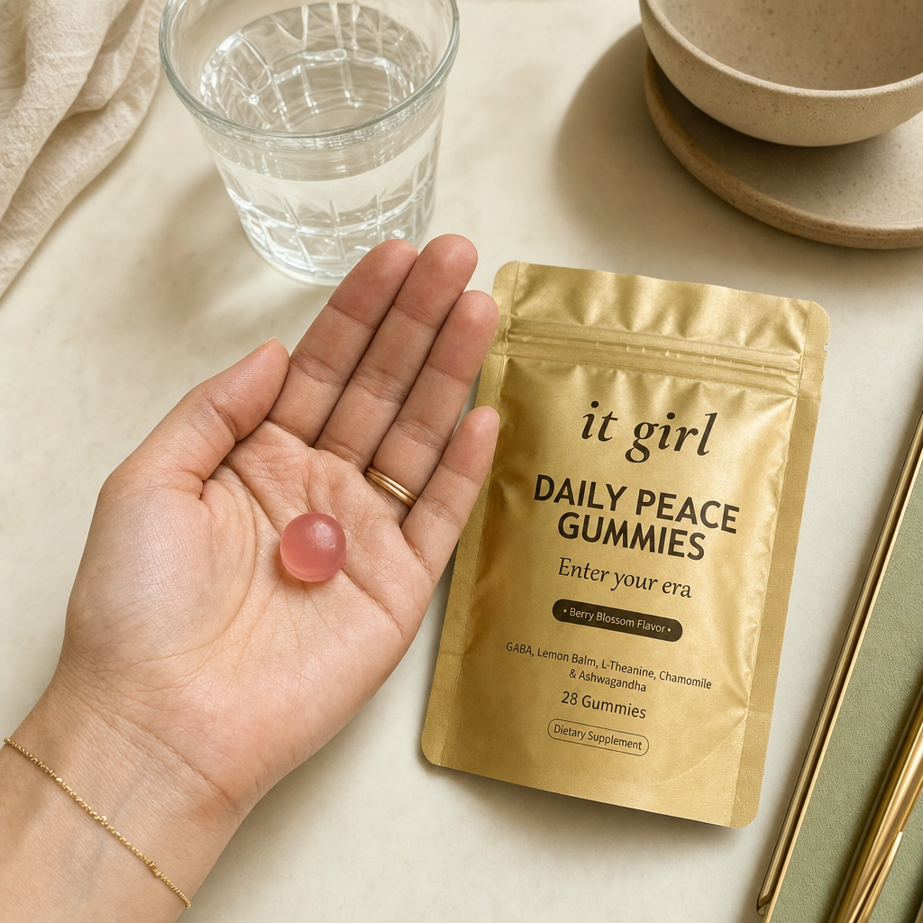 Open palm holding a single pink Daily Peace gummy beside the gold pouch and a glass of water on a cream surface, the GABA and L-Theanine calm signal