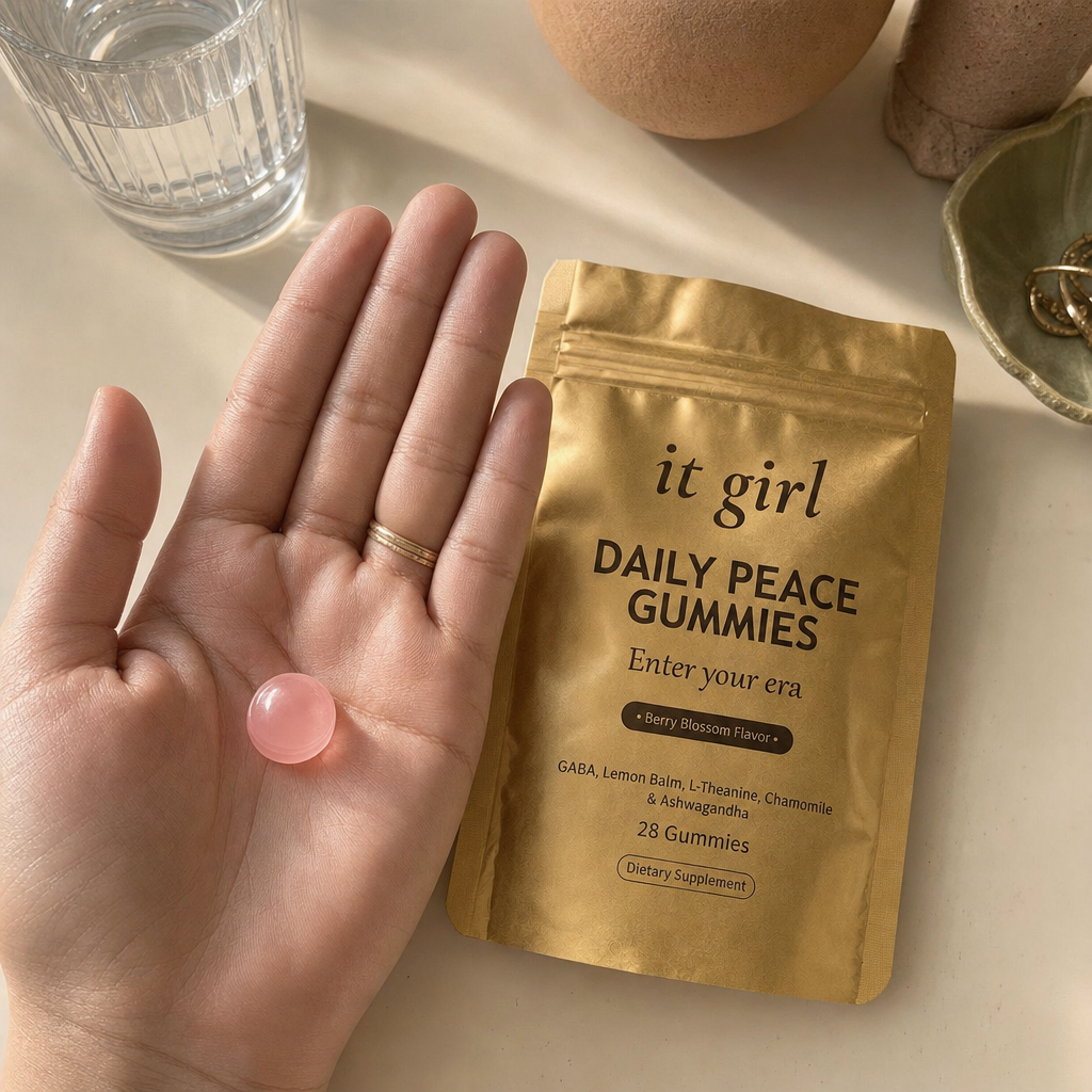 Open palm holding a single pink Daily Peace gummy beside the gold pouch and a glass of water on a cream surface, the GABA and L-Theanine calm signal