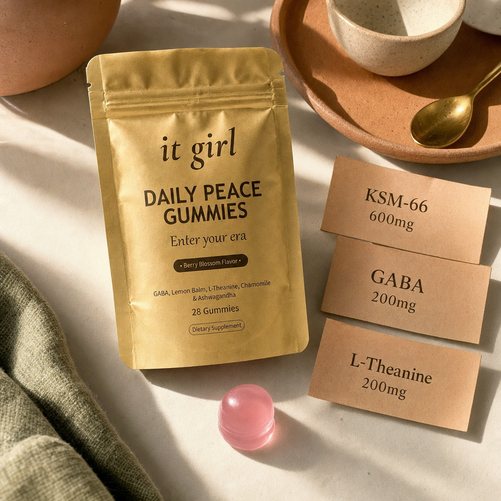 Warm product reveal of the gold It Girl Daily Peace pouch beside a single gummy and three dose cards reading GABA 200mg, L-Theanine 200mg, KSM-66 600mg, the full studied stack