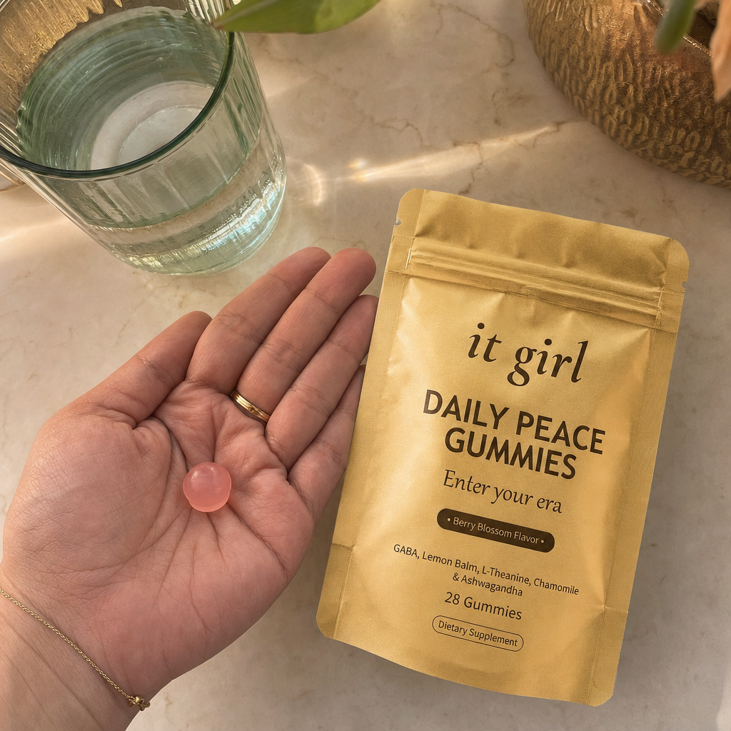 A single pink Daily Peace gummy in an open palm beside the gold pouch and a glass of water on a warm cream counter in early-evening light, calm not sedation, the same evening