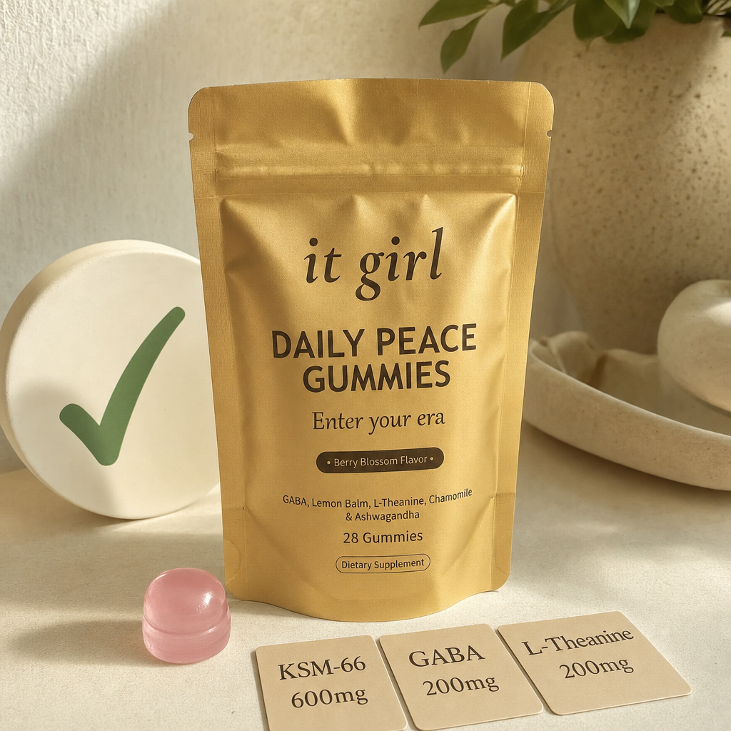 The real matte-gold It Girl Daily Peace pouch with a green checkmark, a single pink gummy, and three dose cards reading KSM-66 600mg, GABA 200mg, L-Theanine 200mg on a warm cream surface, the right vehicle