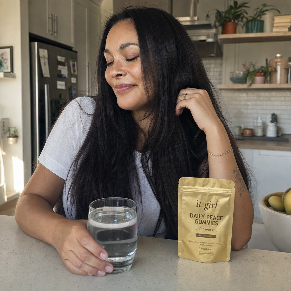 Warm candid of the same woman calm and present at her evening counter with a glass of water and the gold Daily Peace pouch nearby, taking an easy exhale instead of pouring a drink