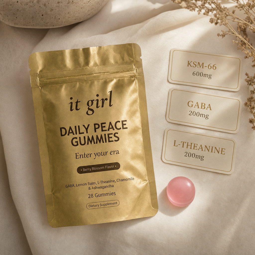 The real matte gold It Girl Daily Peace pouch and a single pink gummy beside three dose cards: KSM-66 600mg, GABA 200mg, L-Theanine 200mg.