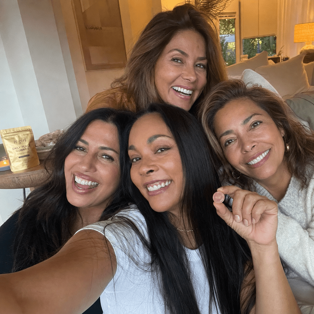 Warm candid selfie of several professional women forty to fifty-five with tea and water in the evening, a Daily Peace pouch resting subtly nearby, no wine