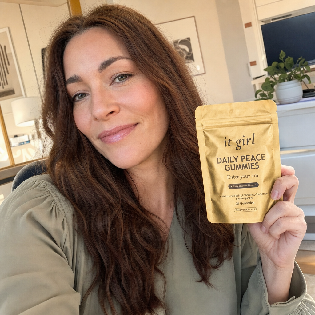 Lauren Hartley taking a warm phone selfie holding the matte gold It Girl Daily Peace pouch up by her face at her office desk, the one formula that passed the audit