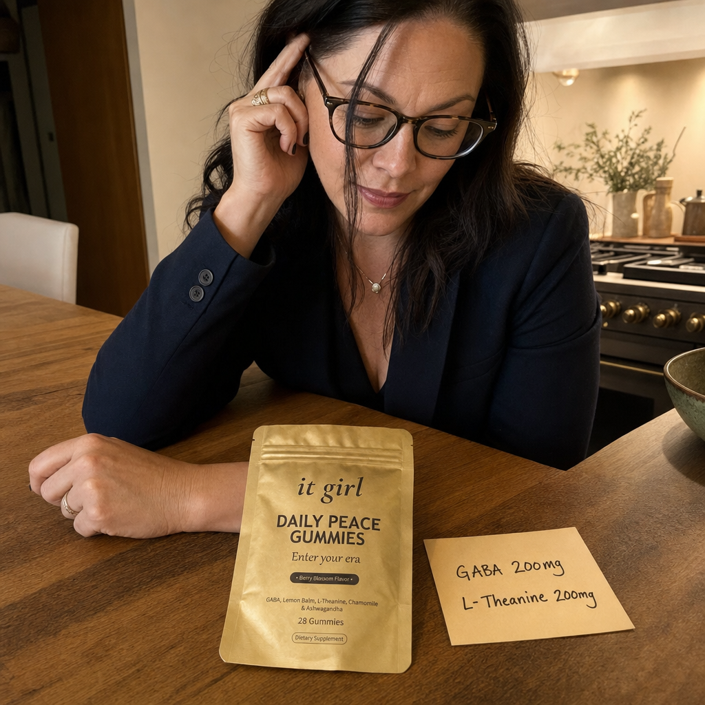 Lauren Hartley in a dark blazer at her kitchen counter looking down at the small matte-gold It Girl Daily Peace pouch lying flat on the counter, the brand she chose to take herself after the test