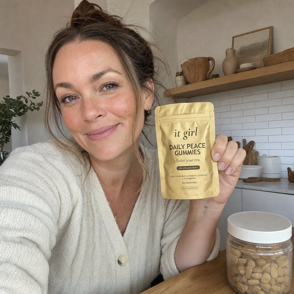 A relieved woman holding up the gold It Girl Daily Peace pouch toward the camera at her kitchen table, with one generic jar set aside