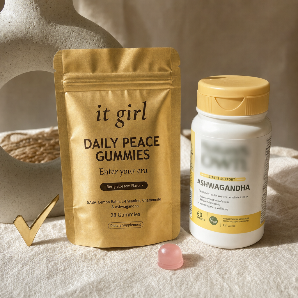 Real side-by-side product photo on a soft cream surface, the matte soft-gold It Girl Daily Peace pouch on the left with a gold check beside it, a Nature's Own style ashwagandha bottle on the right with its brand name blurred, It Girl the blend built for women versus the single-ingredient one