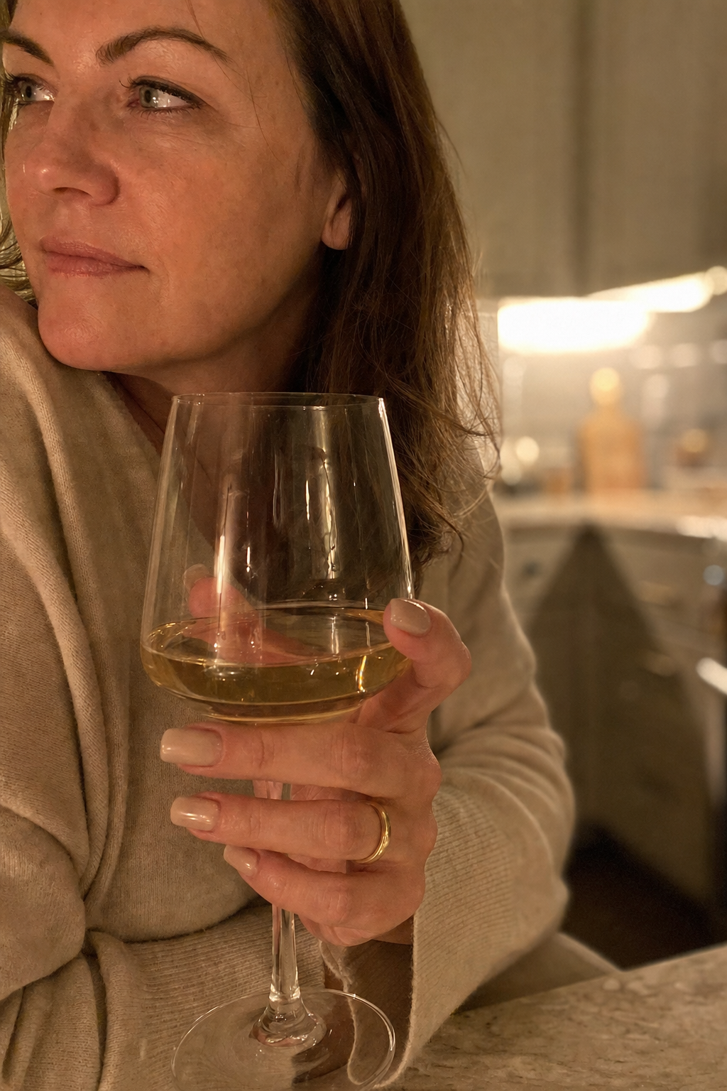 Warm macro of a woman's hand wrapped around the stem of a wine glass in gold evening light, the wine glowing, a contemplative and quiet moment, the reach for the calm signal inside the glass