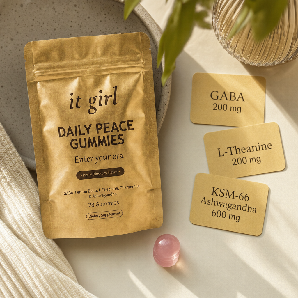 The real matte gold It Girl Daily Peace pouch on warm cream beside three dose cards reading GABA 200mg, L-Theanine 200mg, and KSM-66 Ashwagandha 600mg and a single pink gummy, the formula that hands the calm signal back directly