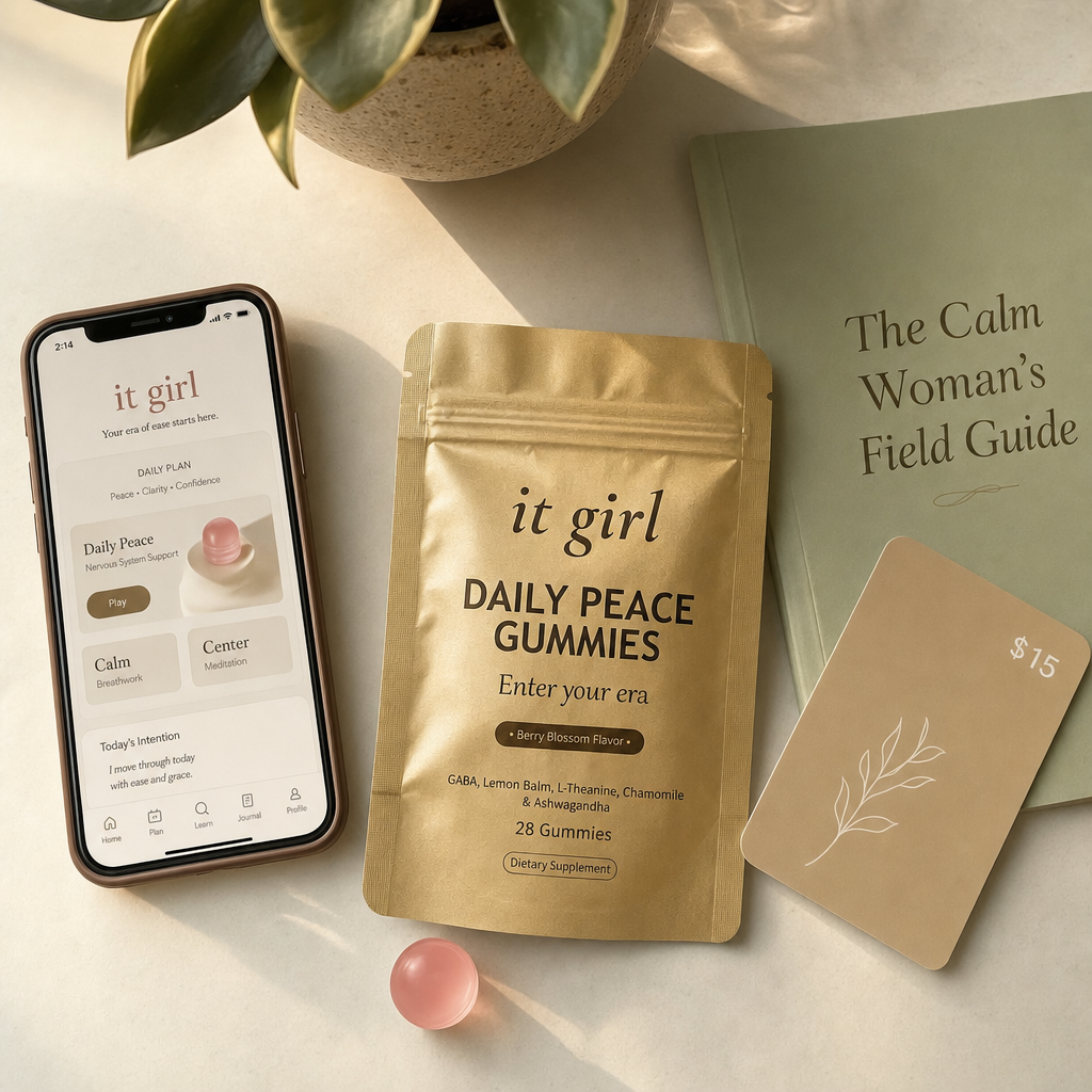 The real It Girl Daily Peace bundle on warm cream, the gold pouch front and center with the It Girl app on a phone, the Calm Woman's Field Guide booklet and a fifteen-dollar gift card, a whole month of calm for about a dollar a day