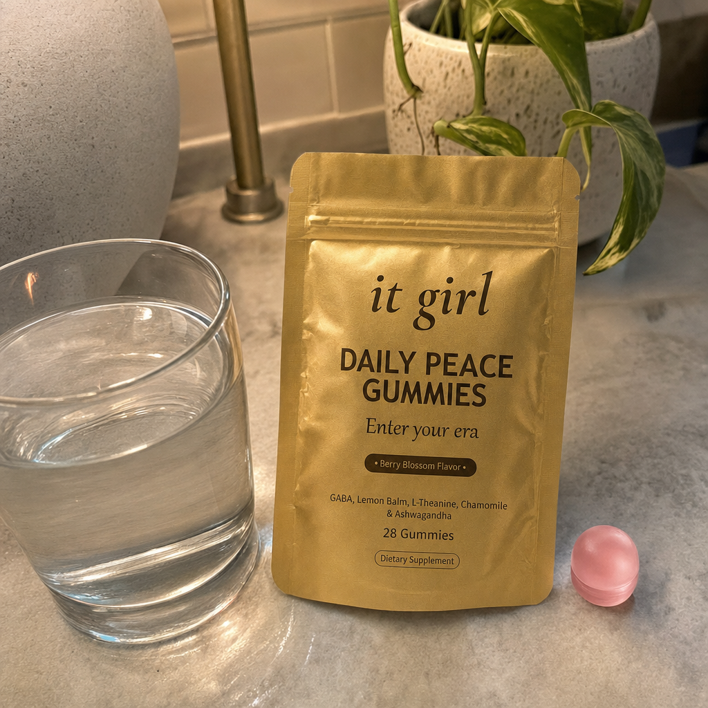 The real It Girl Daily Peace pouch resting on a warm evening kitchen counter beside one glass of water, the tired end-of-day reach answered by the signal itself instead of a glass of wine