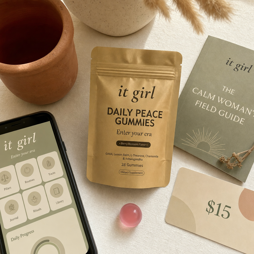 The real It Girl Daily Peace bundle on warm cream, the gold pouch front and center with the It Girl app on a phone, the Calm Woman's Field Guide booklet and a fifteen-dollar gift card, a whole month of calm for about a dollar a day
