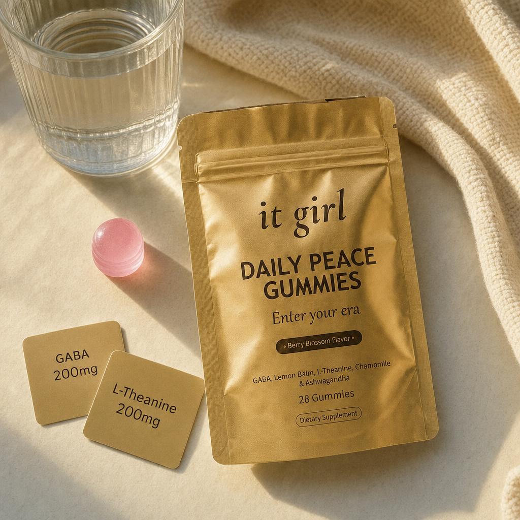 The real It Girl Daily Peace pouch laid open with one pink gummy beside it and two warm dose cards reading GABA 200mg and L-Theanine 200mg on a cream surface in soft evening light