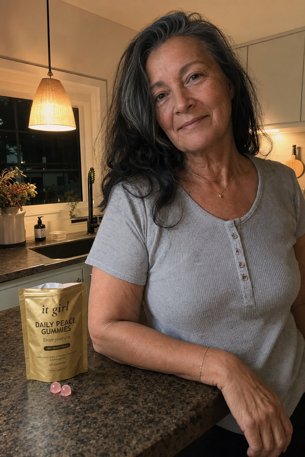 Warm evening kitchen photo of a relaxed woman in her late fifties at ease at the counter with the real gold It Girl Daily Peace pouch resting beside her, top rolled open, the calm she was reaching for handed back directly