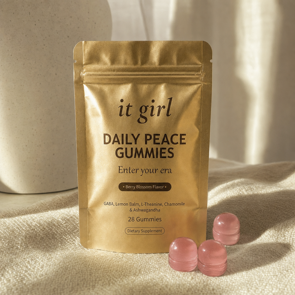 The gold It Girl Daily Peace pouch standing on a cream surface in warm morning light beside its gummies, the studied KSM-66 dose working on cortisol underneath