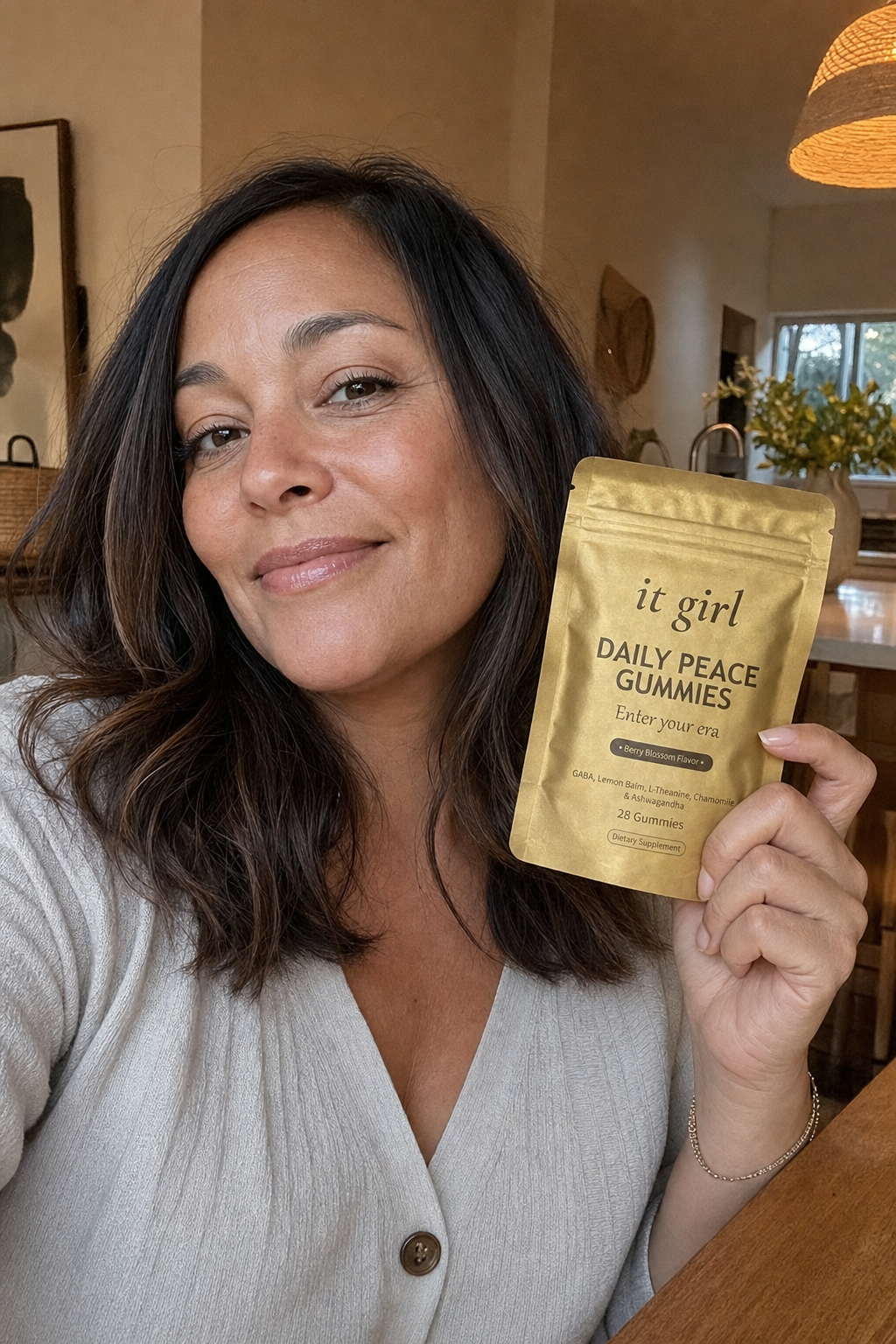 A calm, present woman in her forties at her warm kitchen table holding the real gold It Girl Daily Peace pouch with a relieved half-smile, settled and unbraced