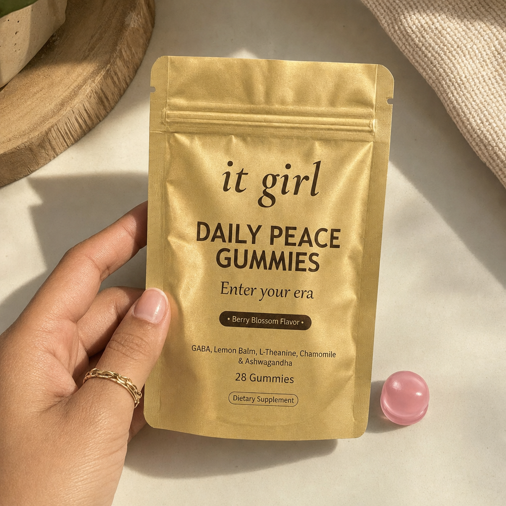 The real matte-gold It Girl Daily Peace pouch in warm daylight on a cream surface beside a single pink gummy, the thing that quiets the reach instead of numbing it