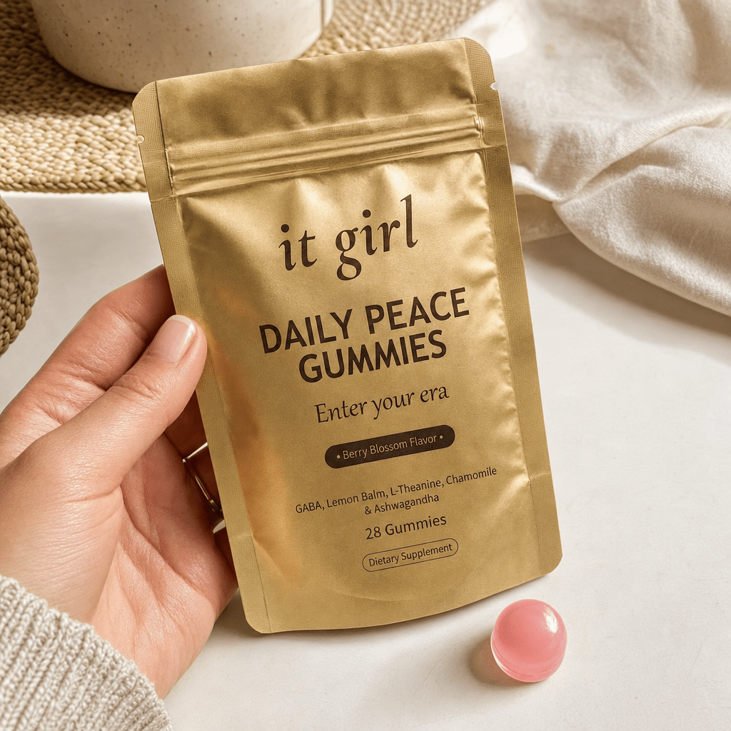 The real matte-gold It Girl Daily Peace pouch in warm daylight on a cream surface beside a single pink gummy, the thing built to rebuild the buffer rather than numb it