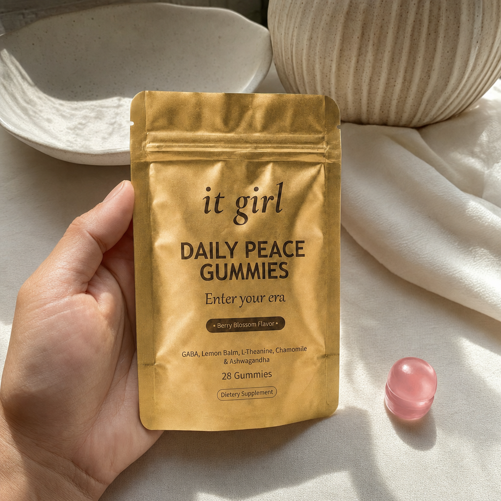 The real matte-gold It Girl Daily Peace pouch in warm daylight on a cream surface beside a single pink gummy, the thing built to rebuild the buffer rather than numb it