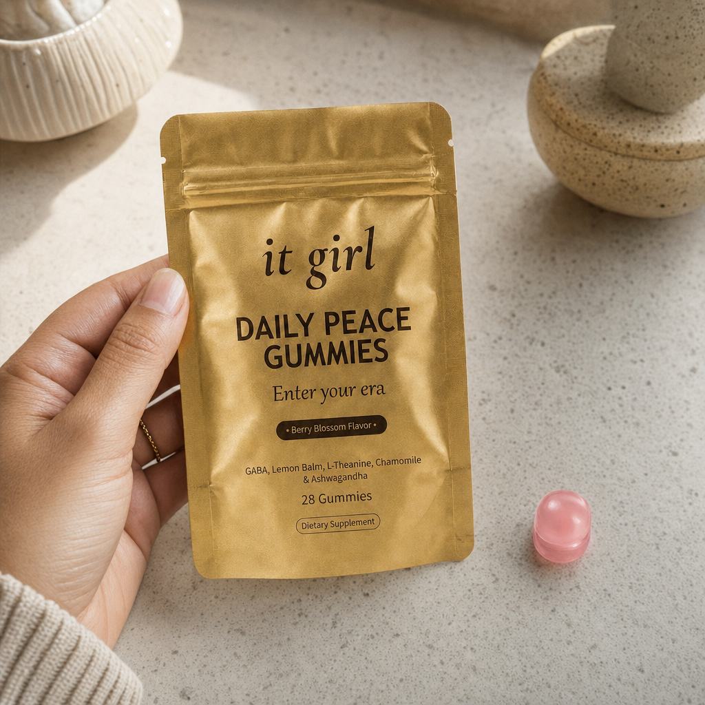 The real matte-gold It Girl Daily Peace pouch in warm daylight on a cream surface beside a single pink gummy, the thing built to rebuild the buffer rather than numb it