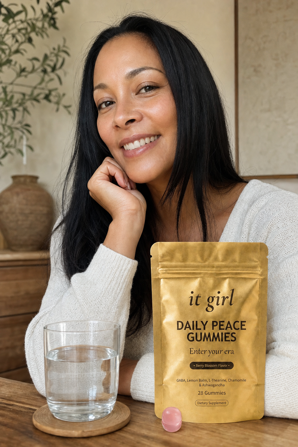 Ultra-realistic candid photo: a woman about 40 standing easy and genuinely light, shoulders down, a real relaxed smile in a calm warm home, the real matte-gold It Girl Daily Peace pouch and a glass of water on a nearby surface in soft daylight