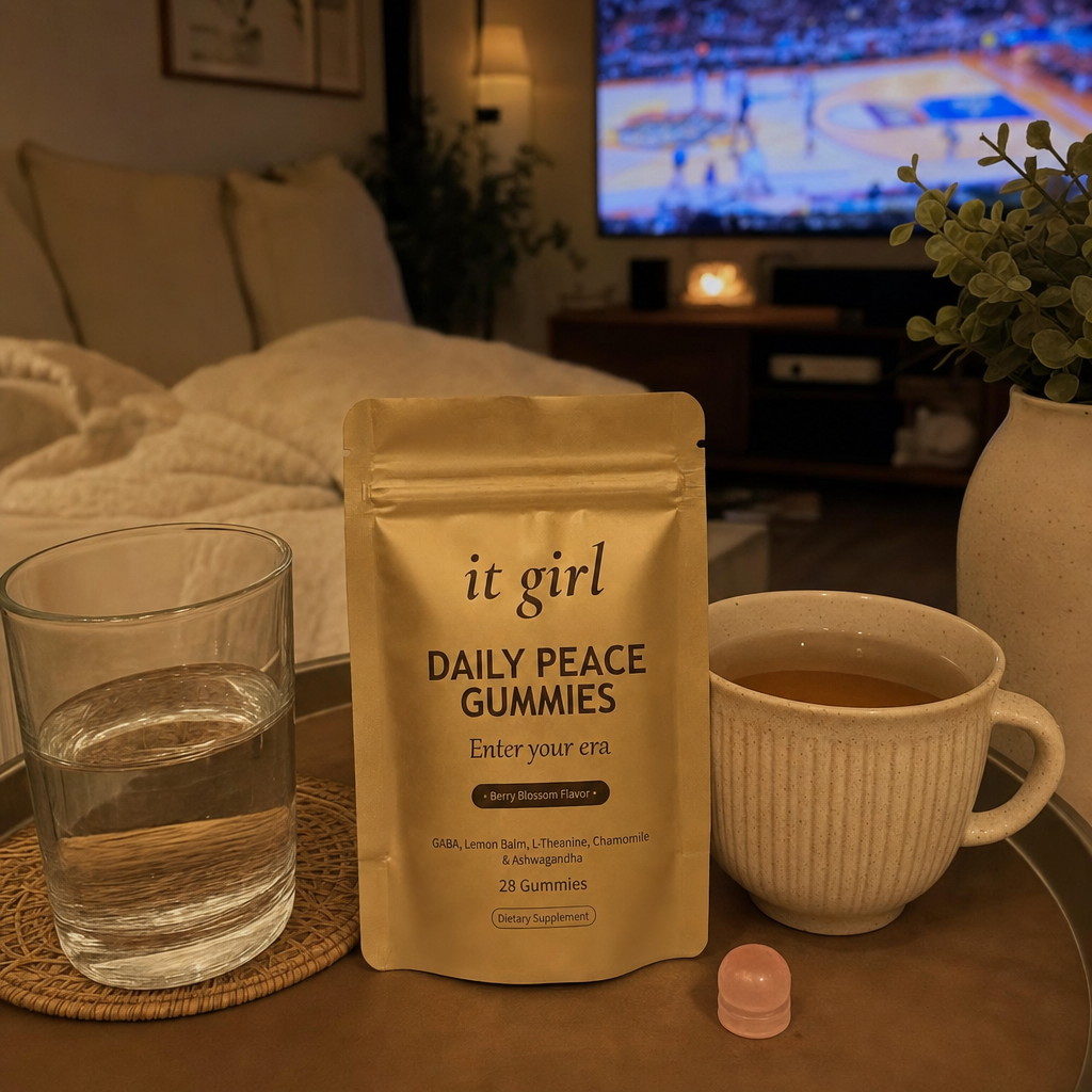 Quiet early-evening living room with the game softly on the TV, a warm cup of tea and the gold Daily Peace pouch on the side table, the calm of an evening that is finally hers, no people