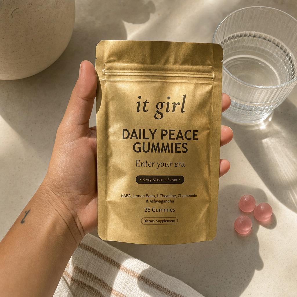 The real It Girl Daily Peace pouch held at palm scale with a few pink gummies and a glass of water in soft daylight