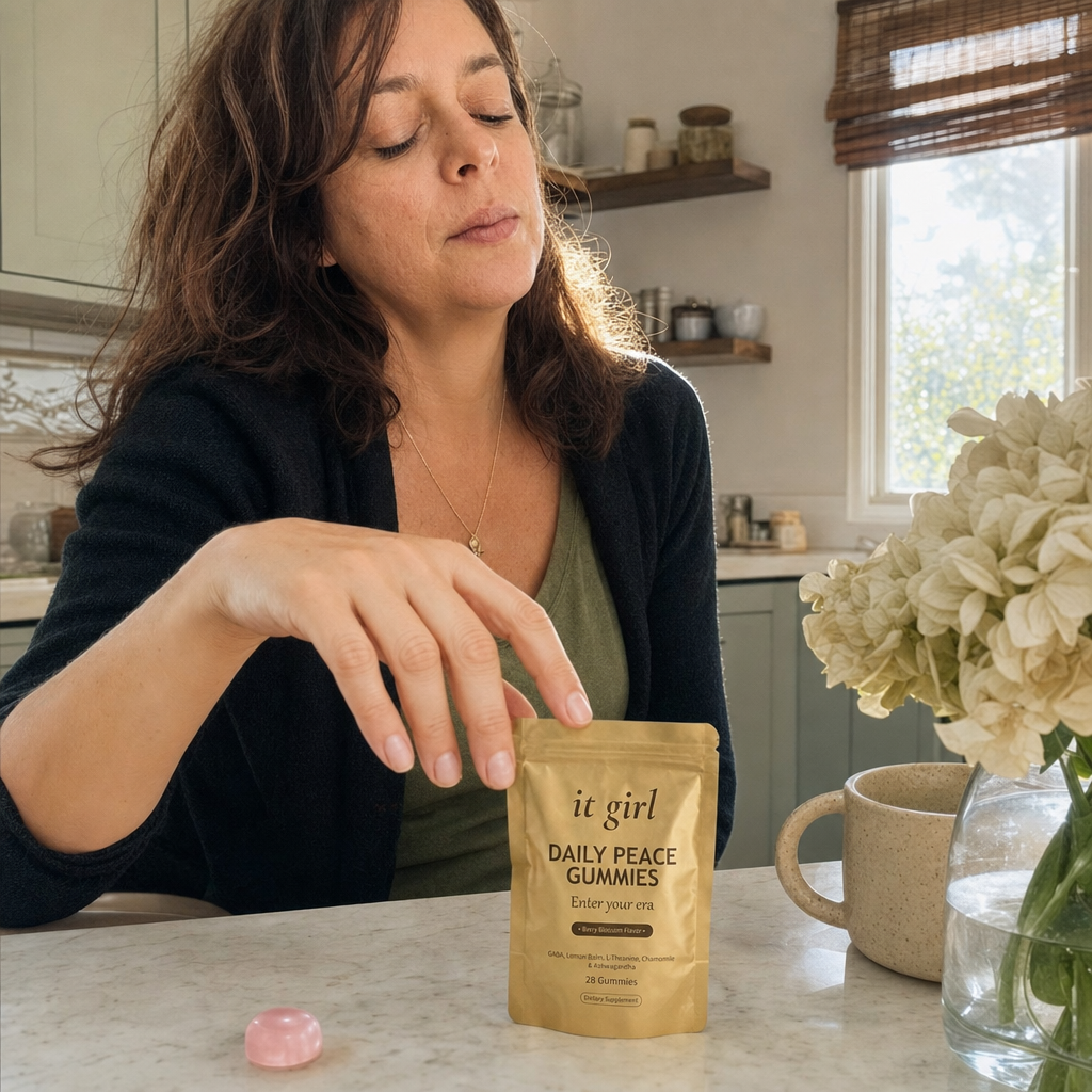 The real soft-gold It Girl Daily Peace pouch beside a single pink gummy and a glass of water on a warm cream surface, the calm signal handed over clean