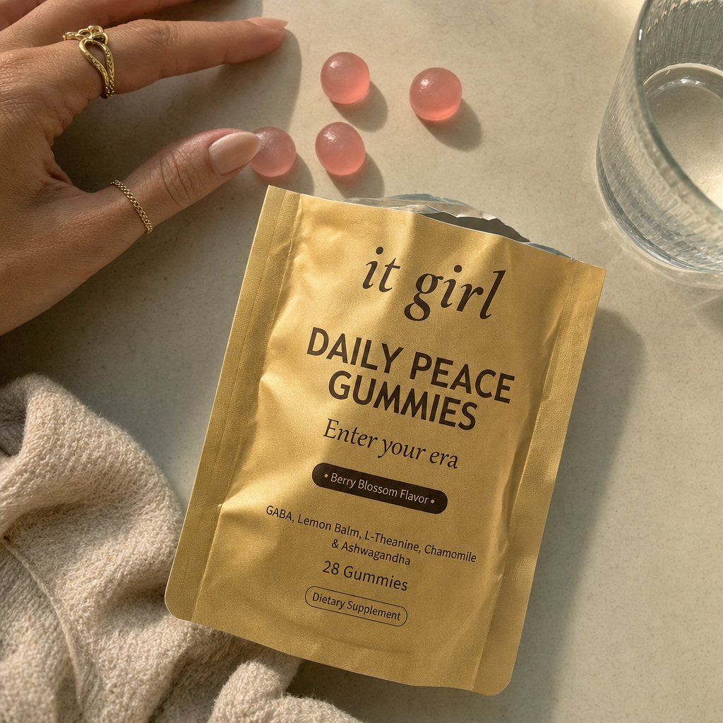 A warm real photo of the gold It Girl Daily Peace pouch torn open with a few berry-blossom gummies spilled beside a glass of water, the calm signal handed back clean