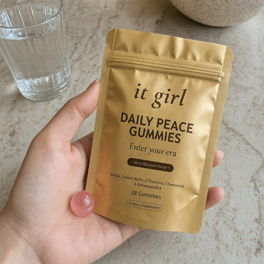 A single pink Daily Peace gummy in an open palm beside the gold pouch and a glass of water on a warm cream counter in early-evening light, calm not sedation, the same evening