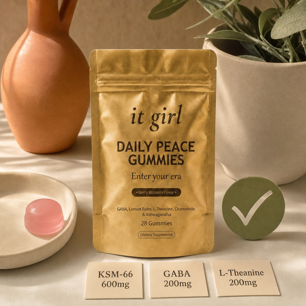 The real matte-gold It Girl Daily Peace pouch with a green checkmark, a single pink gummy, and three dose cards reading KSM-66 600mg, GABA 200mg, L-Theanine 200mg on a warm cream surface, the piece the routine was missing