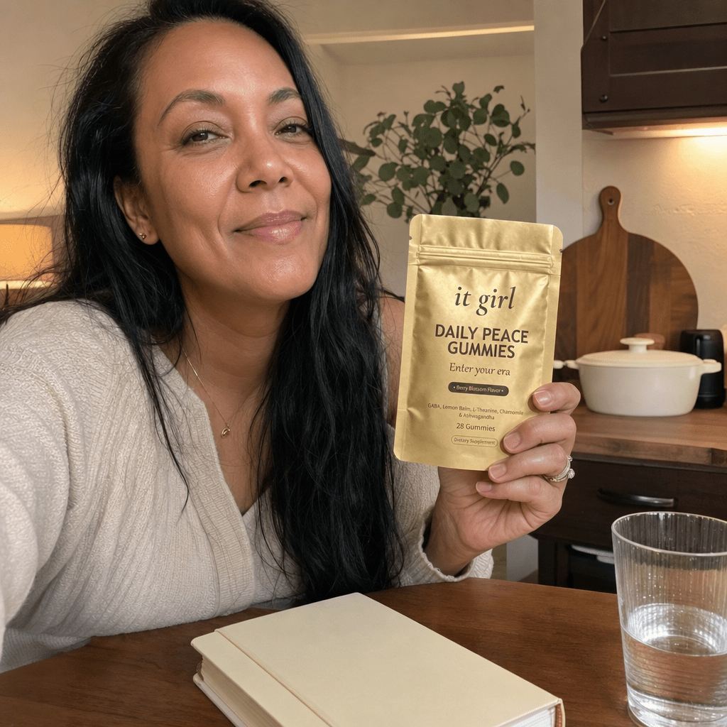 Relieved woman 40 to 55 at her kitchen counter in soft evening light calmly holding the gold It Girl Daily Peace pouch, the studied-dose answer to the same need
