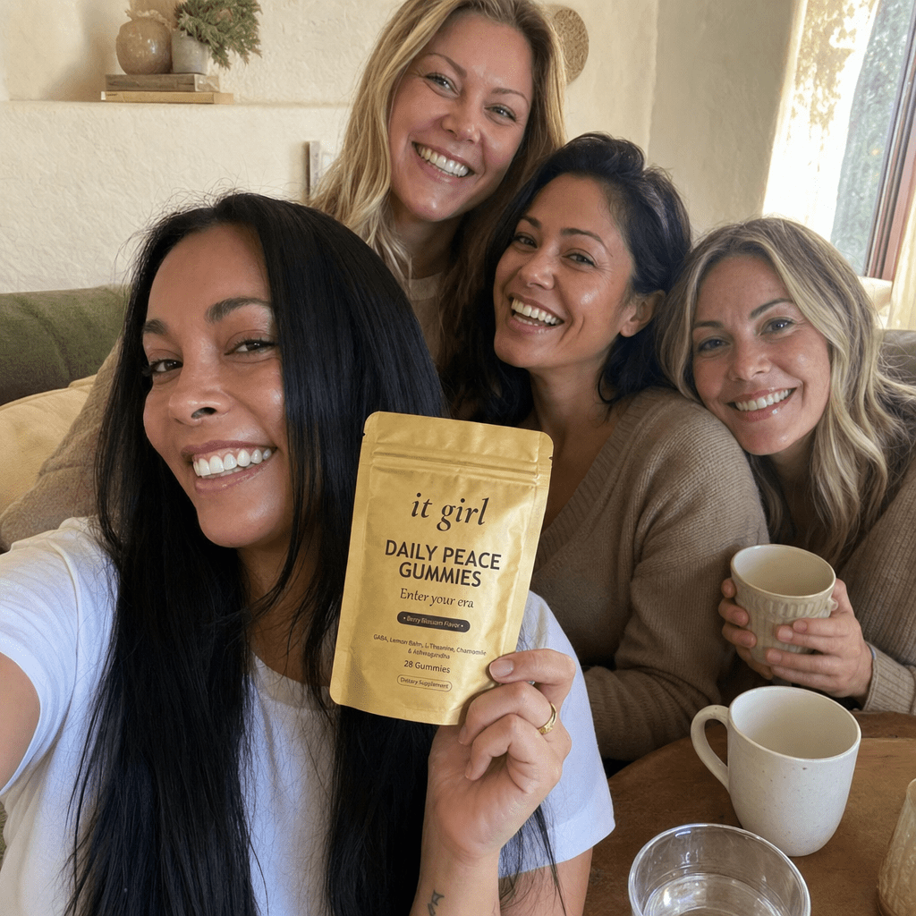 A warm group selfie of several women laughing together, one holding up the gold It Girl Daily Peace pouch they all share