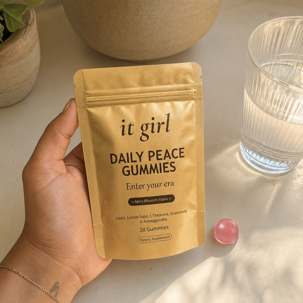 The real gold It Girl Daily Peace pouch and a single pink gummy beside a glass of water in warm light, the same calm signal reached without the wine