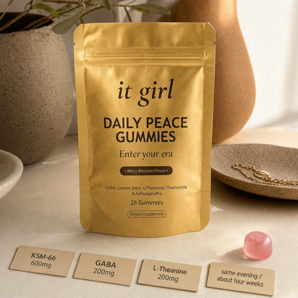 The real matte-gold It Girl Daily Peace pouch with a single pink gummy, three dose cards reading KSM-66 600mg, GABA 200mg, L-Theanine 200mg, and a small timeline card reading same evening and about four weeks, on a warm cream surface