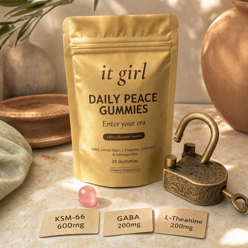 The real matte-gold It Girl Daily Peace pouch with a single pink gummy and three dose cards reading KSM-66 600mg, GABA 200mg, L-Theanine 200mg on cream marble, beside the brass lock now turning clean and open in warm gold, the key cut for the same lock