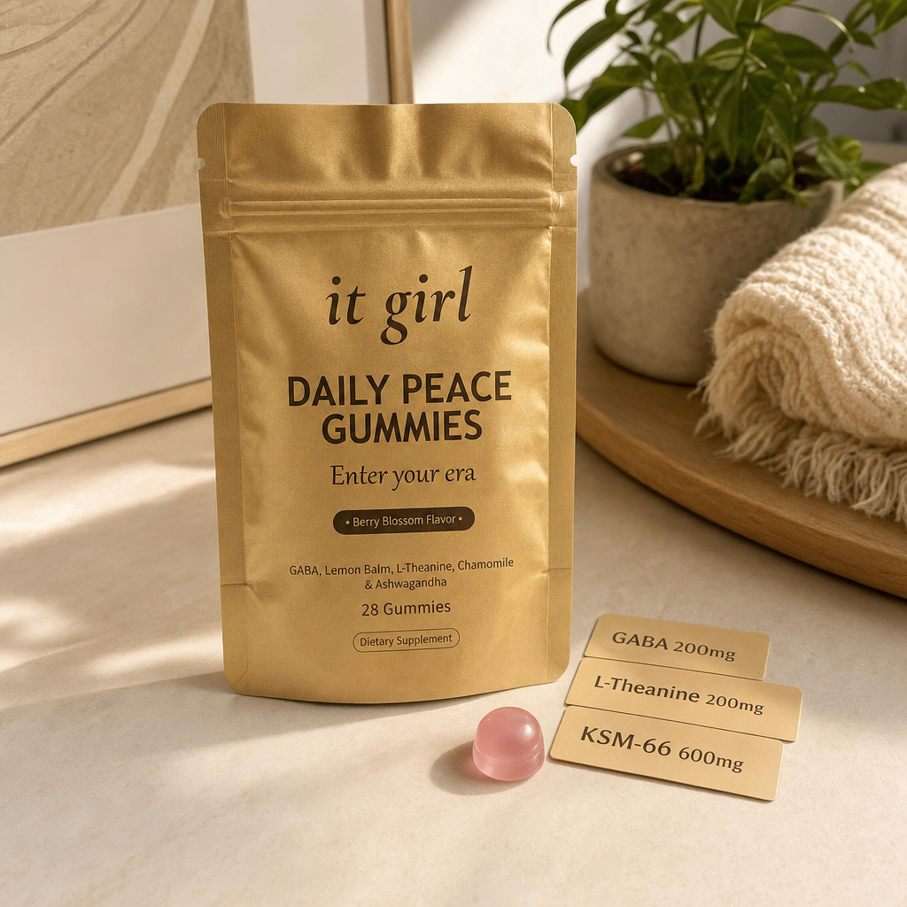 The real matte gold It Girl Daily Peace pouch on a warm cream surface beside a single pink gummy and three named dose cards, GABA 200mg, L-Theanine 200mg, KSM-66 600mg, the studied stack named on the label