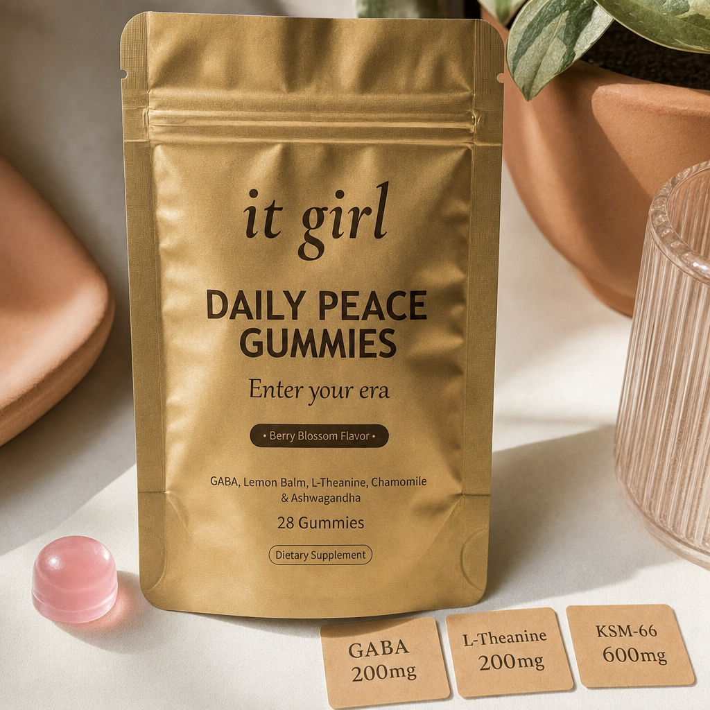 Warm still life of the gold It Girl Daily Peace pouch beside a single pink gummy and three dose cards reading GABA 200mg, L-Theanine 200mg, KSM-66 600mg, the studied stack