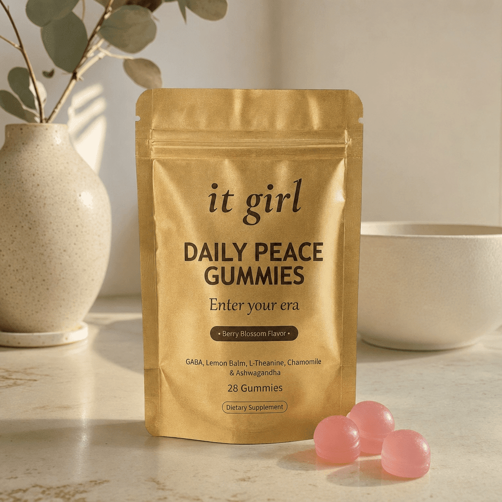 The gold It Girl Daily Peace pouch standing on a cream surface in warm morning light beside its gummies, the studied KSM-66 dose working on cortisol underneath