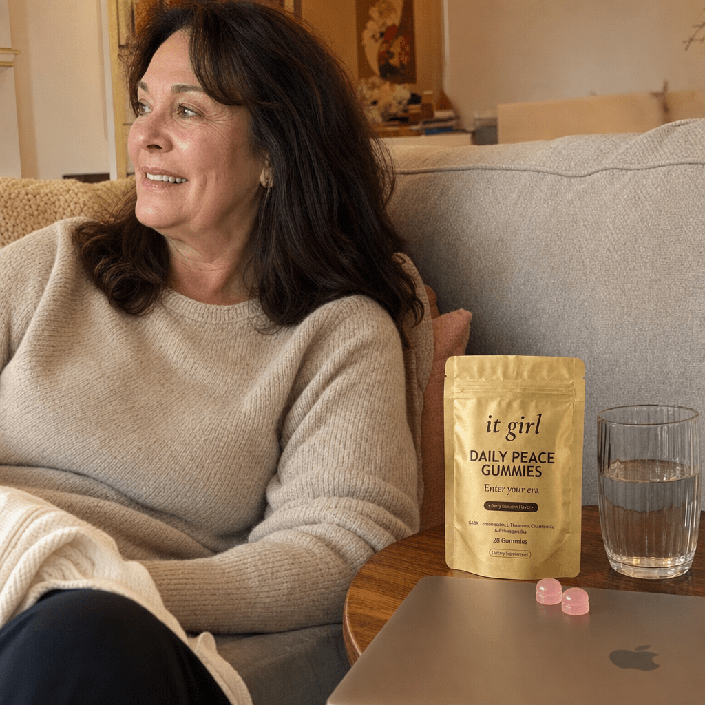 A relaxed woman in her fifties on her couch with the laptop closed, the real gold It Girl Daily Peace pouch and two gummies on the side table, no wine in frame