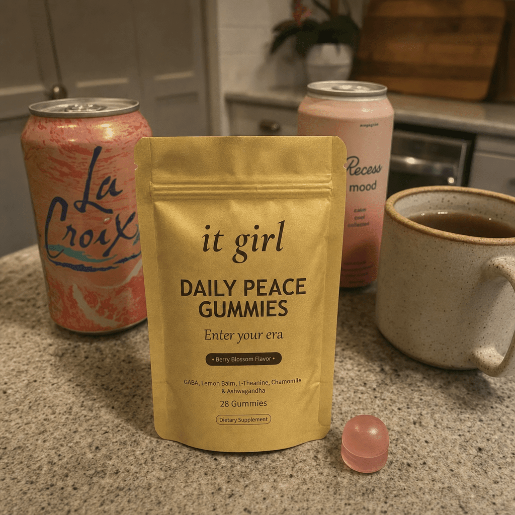 The real matte gold It Girl Daily Peace pouch forward in warm focus on a counter, the abandoned wine swaps, a coral LaCroix can and an adaptogen drink and a mug of cold tea, pushed aside behind it