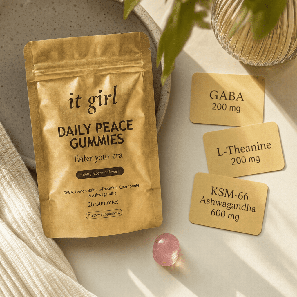 The real matte gold It Girl Daily Peace pouch on warm cream beside three dose cards reading GABA 200mg, L-Theanine 200mg, and KSM-66 Ashwagandha 600mg and a single pink gummy, the formula that hands the calm signal back directly
