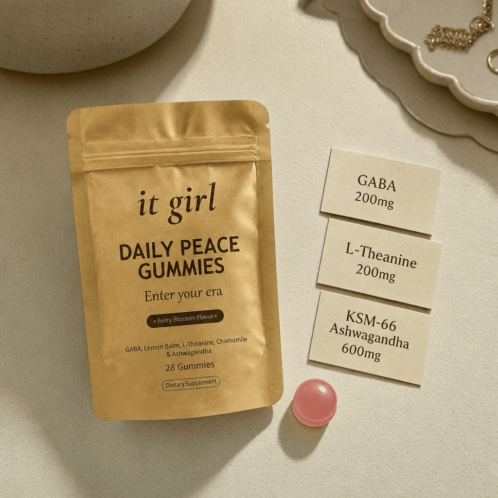 The real matte soft-gold It Girl Daily Peace pouch on warm cream beside three dose cards reading GABA 200mg, L-Theanine 200mg, and KSM-66 Ashwagandha 600mg and a single pink gummy, the formula that hands the calm signal back directly